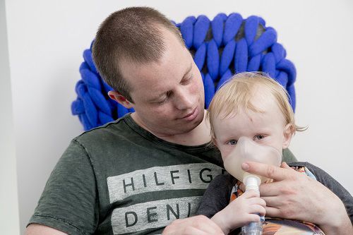 En far der lader sit barn være med til at holde på masken