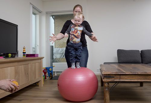 Mor som leger med barnet på en bold i stuen